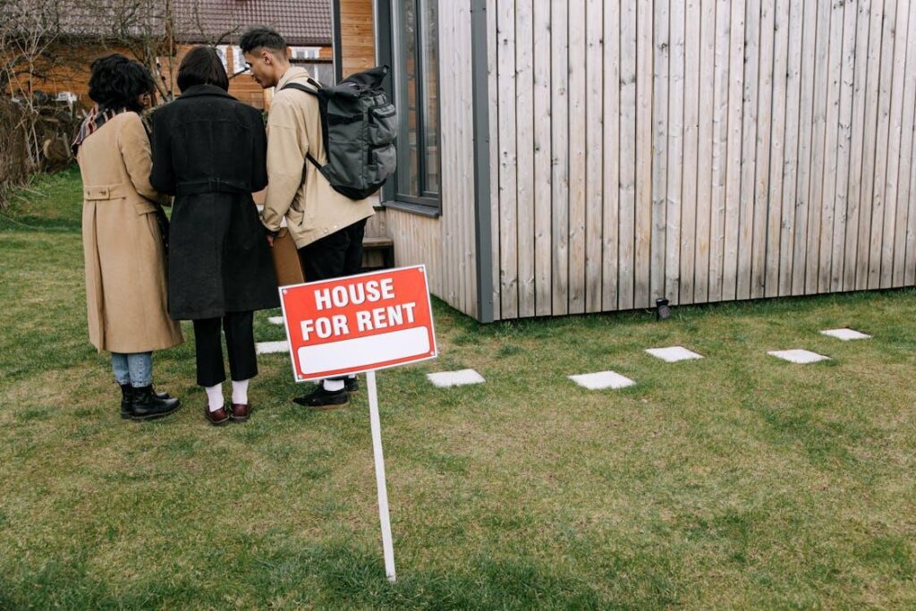 Image of a house for rent sign placed in a front yard with a house and 3 people behind it