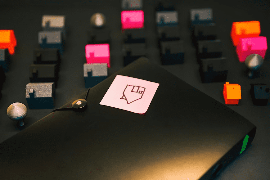 The image shows a collection of colorful keycaps arranged around a black laptop with a sticker on it, possibly related to a keyboard customization or modding theme.
