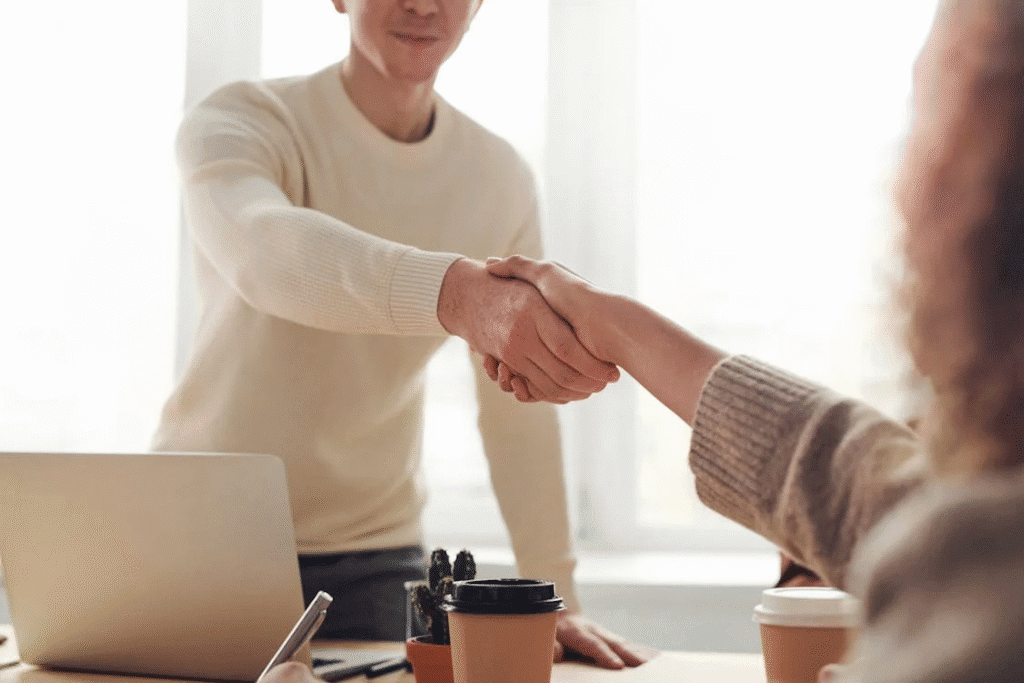 The image shows two people shaking hands, likely in a professional or business setting.
