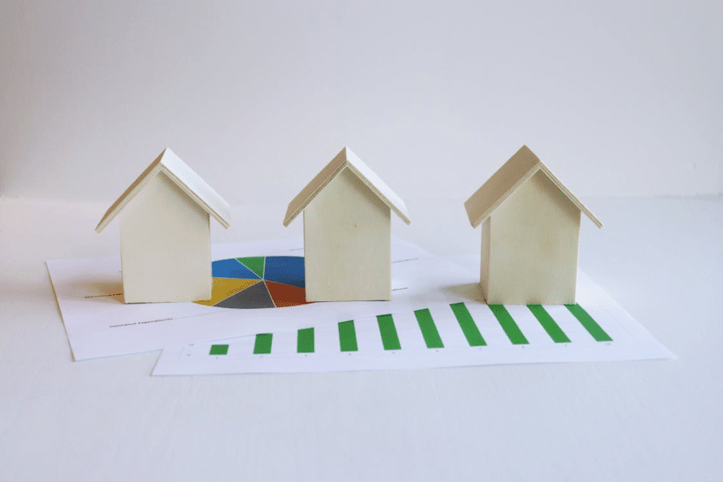 The image shows three small wooden house models placed on top of business charts with graphs and a pie chart, indicating a focus on real estate or market analysis.