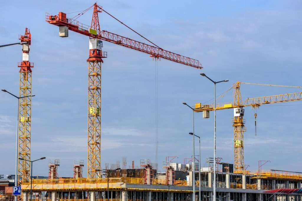 Three tall construction cranes positioned against a clear blue sky