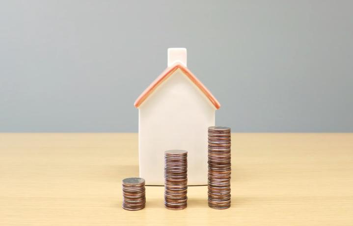 This photo shows a small model house with three stacks of coins in front.