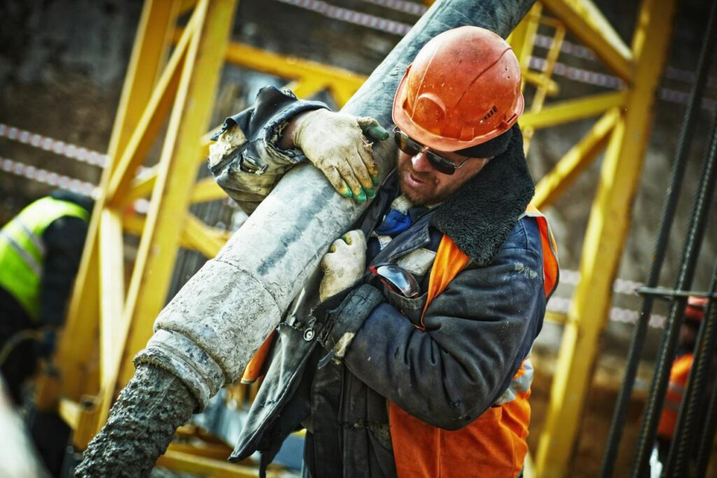 Worker carrying a large pipe across an active construction area