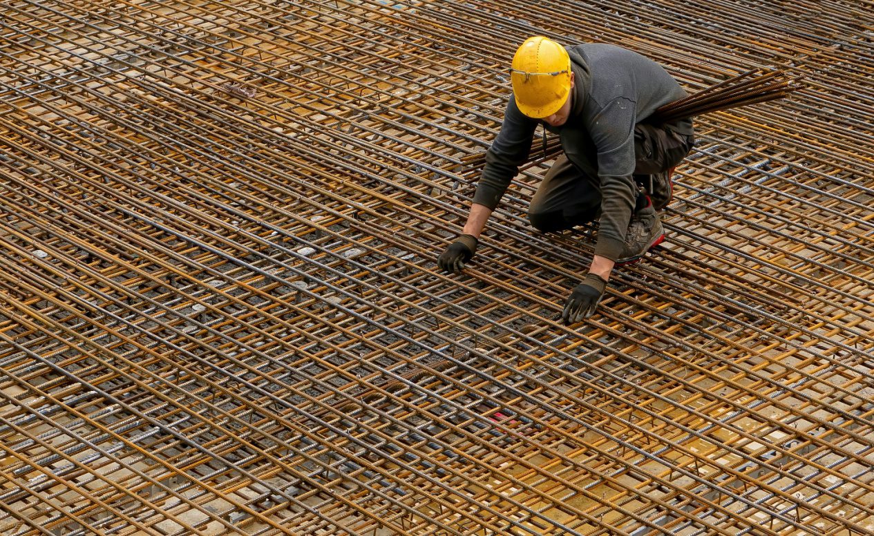 Man wearing a yellow hard hat and black jacket standing on a building frame