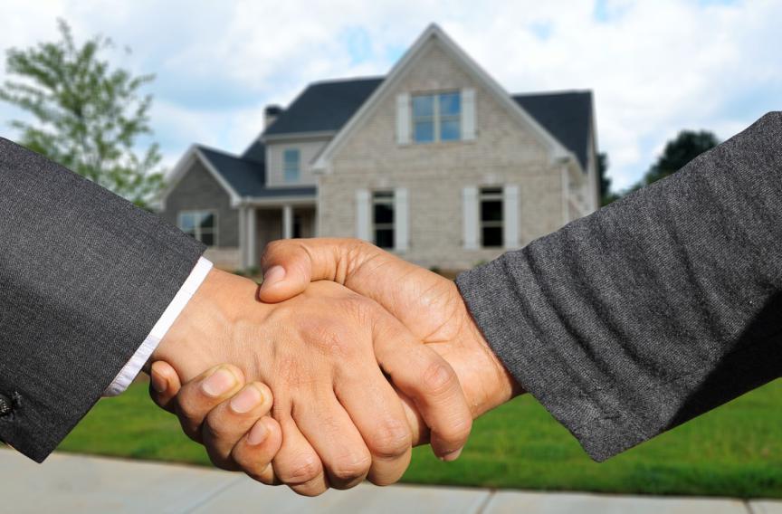 This photo shows two people shaking hands with a house in the background.