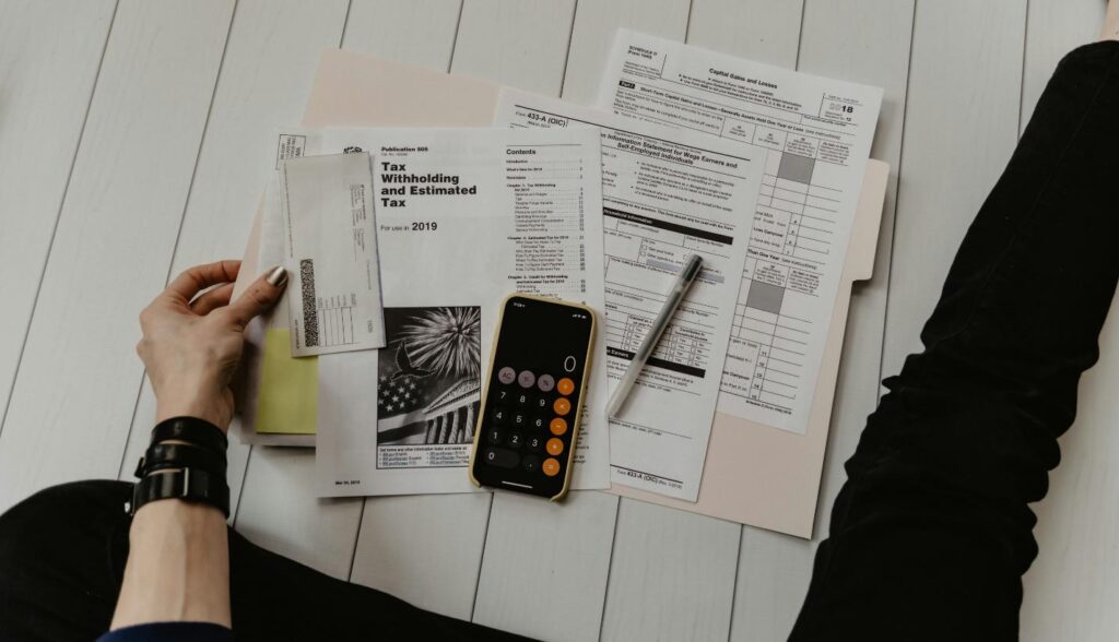 Bird’s eye view of scattered financial documents, a calculator, a pen, and a person’s hand picking up a paper