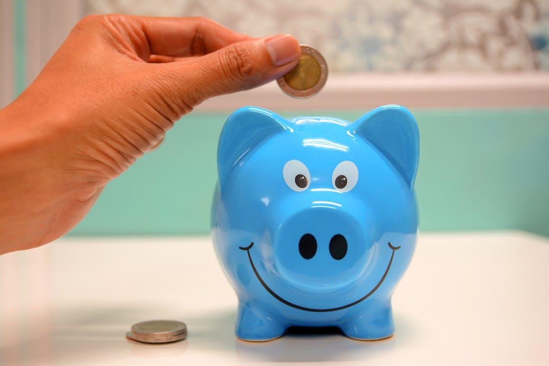 Image of a blue piggy bank and a hand holding a coin poised to drop above it.