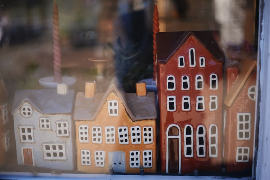 Colorful ceramic house figurines are displayed together in a shop window, resembling a small quaint neighborhood.