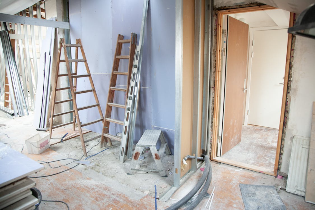 An indoor construction site with unfinished drywall, ladders, tools, and an open doorway during renovation.