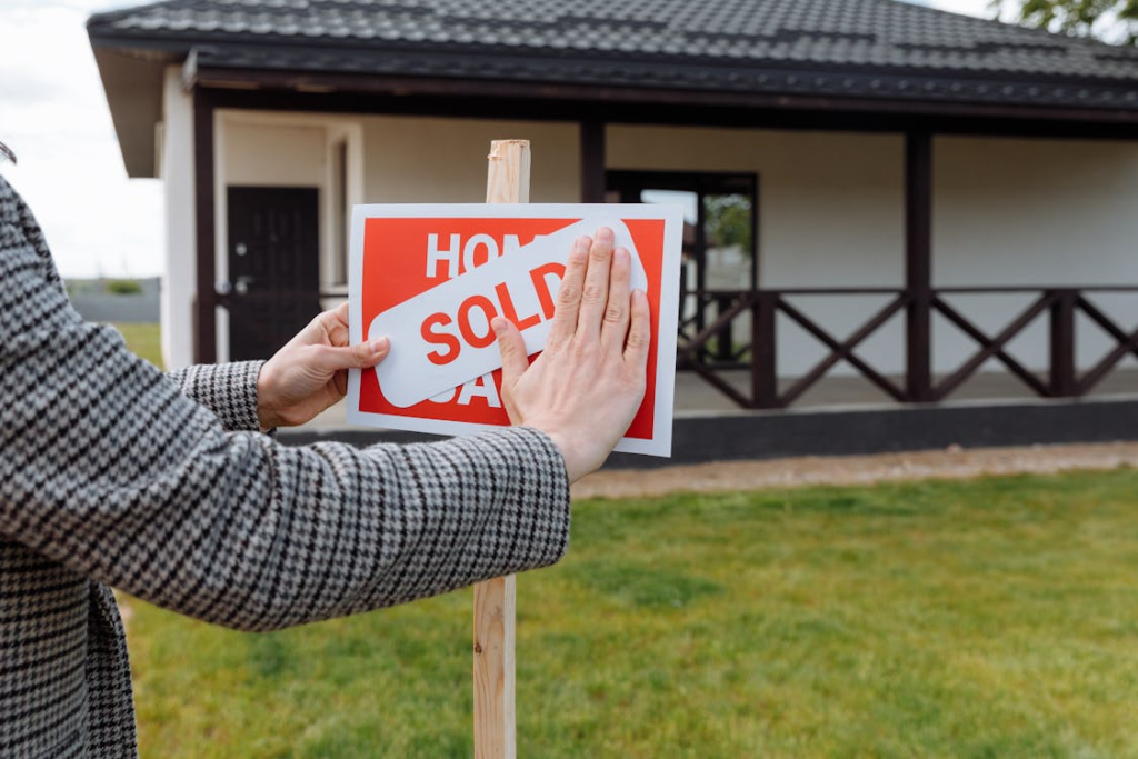 A person placing a “SOLD” sign in front of a house, indicating the property has been sold.