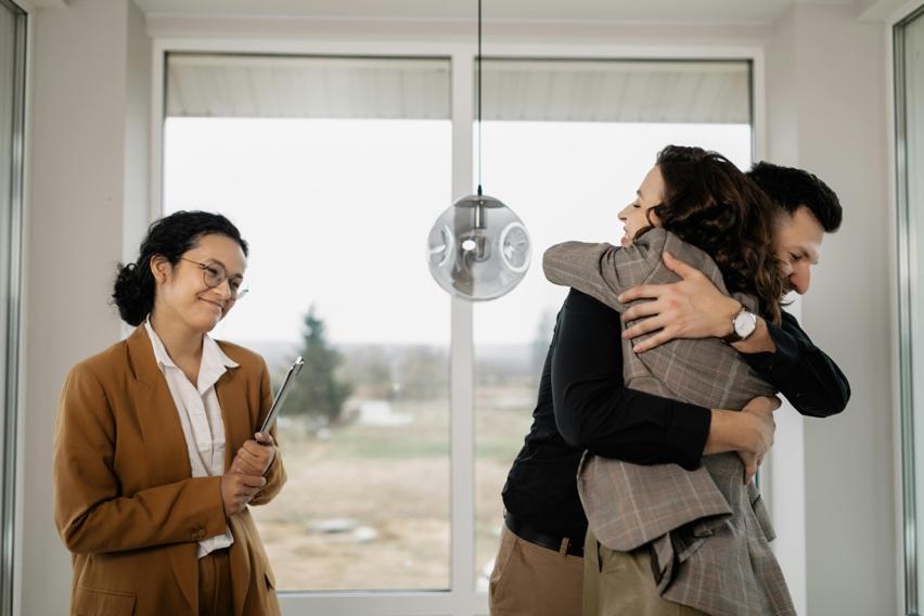 A couple hugging beside a real estate agent after buying a home