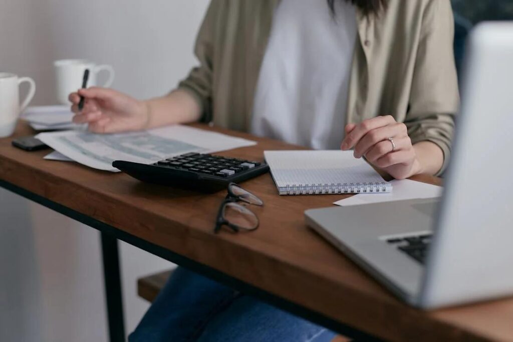 An image of a woman working on her desk with a laptop and a calculator in front of her