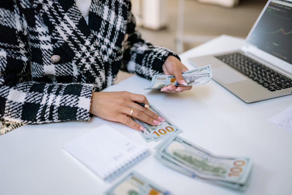 Person counting U.S. dollar bills at a desk with a laptop