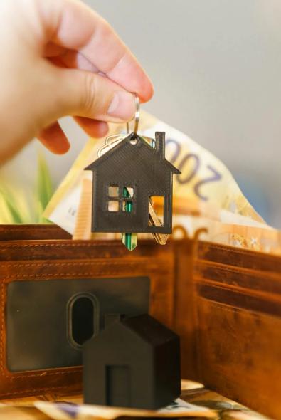 This image shows a brown wallet, a model house, keys, and currency notes