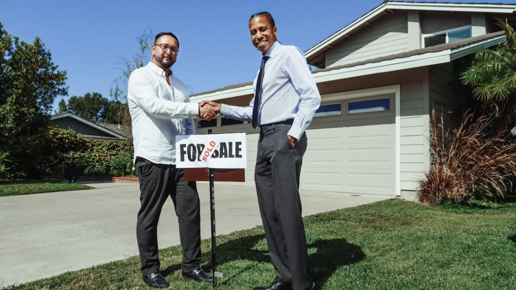 Two men in business attire standing in front of a modern home, engaged in serious discussion about real estate investment