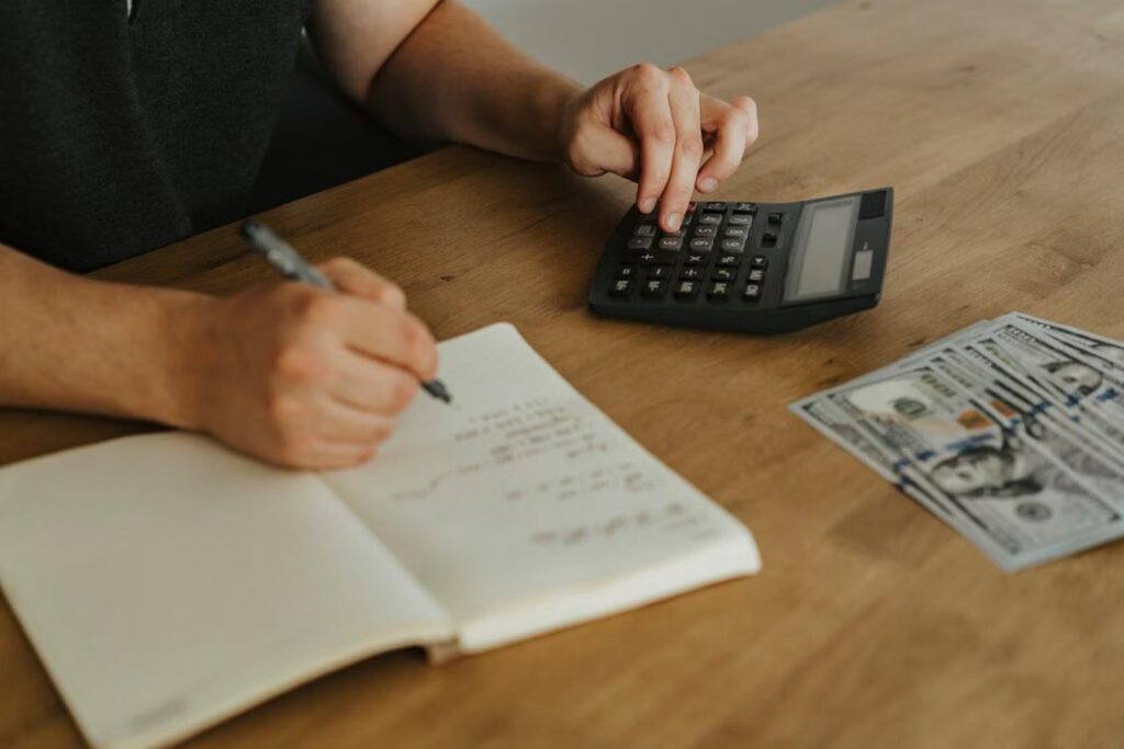 A money is writing on a book while using calculator