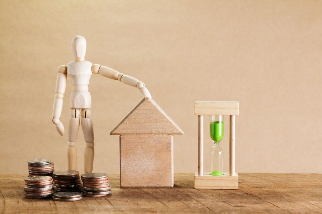 Wooden mannequin with house model, coins, and an hourglass